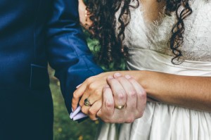 A bride and groom holding hands while wearing wedding rings