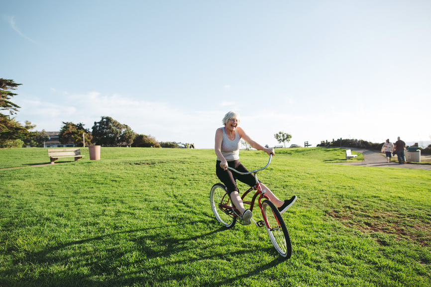 A happy older Swedish woman rides a bike through a field.