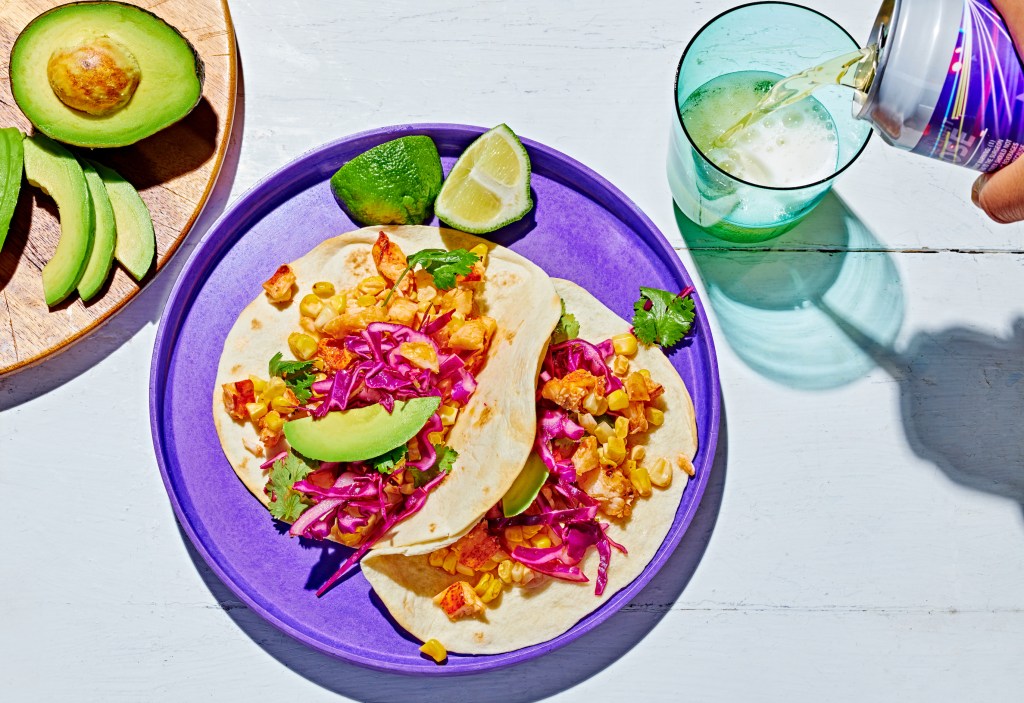 a purple plate holding two grilled lobster and corn tacos topped with avocado and red cabbage