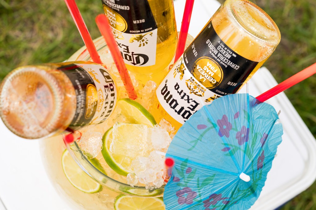 a pitcher of homemade margarita with a few bottles of corona turned upside down in it, finished with limes and a paper umbrella