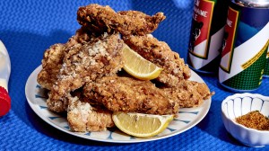 a plate of fried chicken strips with two lemon wedges in front of two cans of beer