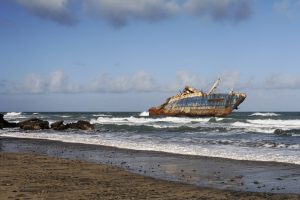 Vom Strand aus ist ein Schiffswrack zu sehen, das im seichten Wasser auf Grund gelaufen ist