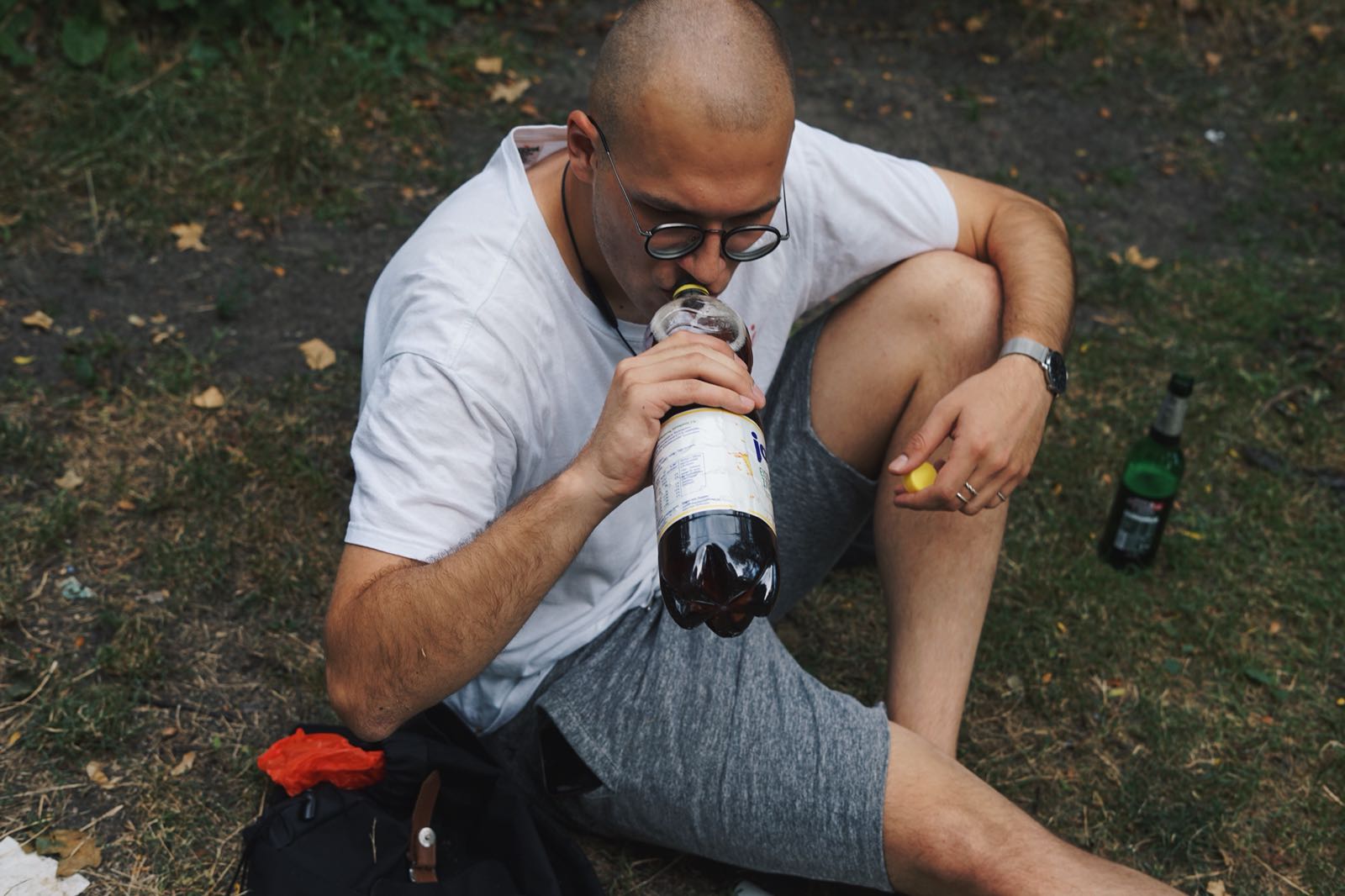 Ein junger Mann hockt im Gras und trinkt Eistee