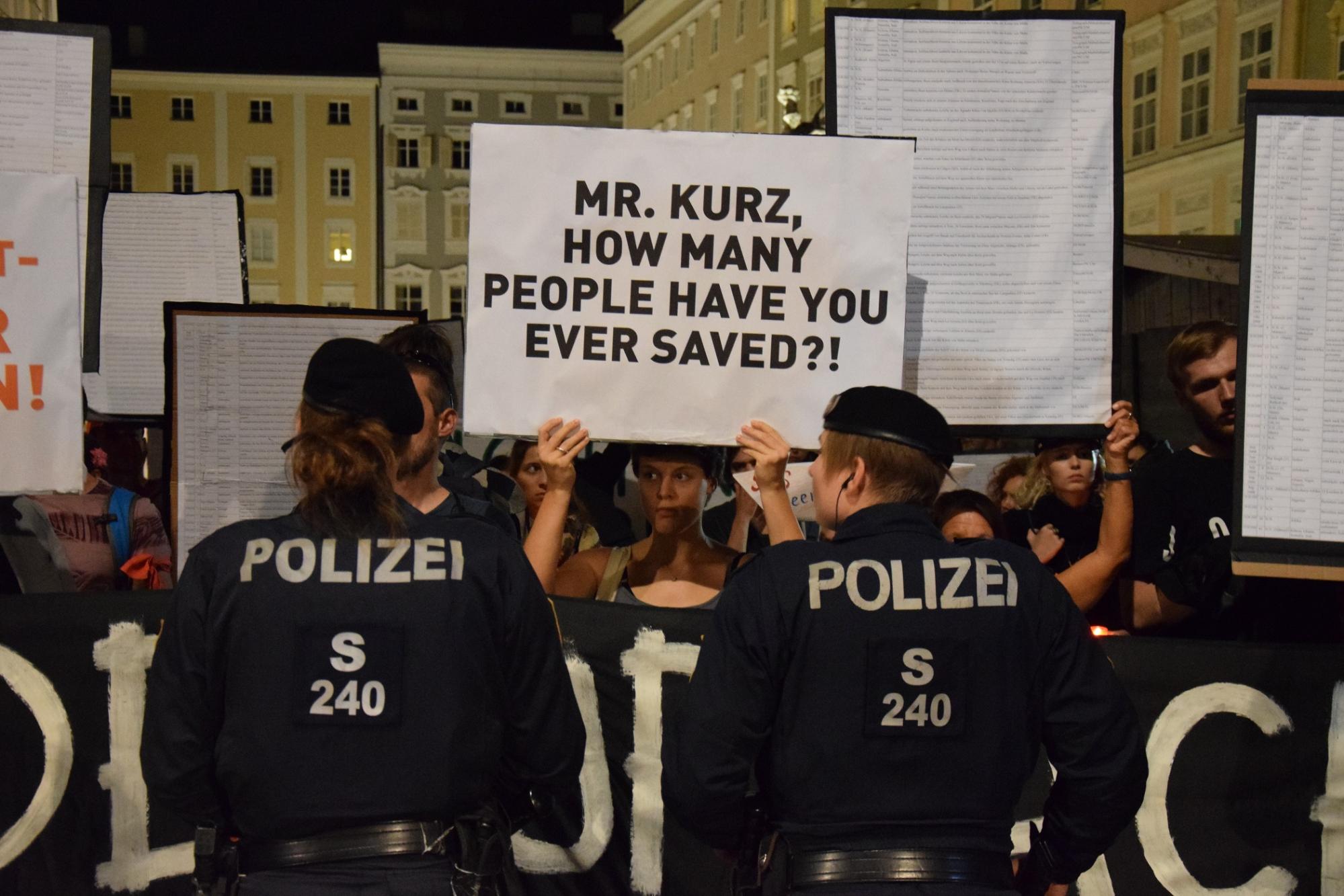 Eine Demonstrantin hält zwischen zwei Einsatzkräften ein Schild hoch: