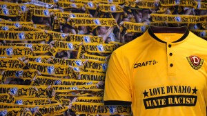 Ein Trikot auf dem "Love Dynamo. Hate Racism" steht vor Fans von Dynamo Dresden