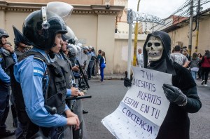 A protester in Honduras dressed as death confronts a police officer.