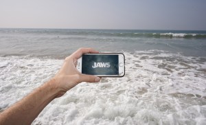 A phone playing 'Jaws' in the surf at a beach