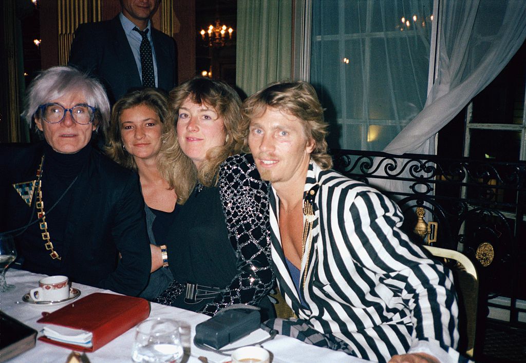 Artist Andy Warhol (1928 - 1987) with fan Catherine Guinness and photographer Christopher Makos (right), Cafe Royal, London, 8th July 1986. Pictured at a dinner party after Anthony d’Offay Gallery opening for Warhol’s ‘Self Portrait’ series. (Photo by Vincent McEvoy/Redferns)