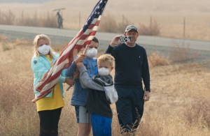 Une famille avec des masques agite un drapeau américain dans un champ.