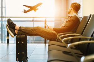 Man sits at airport with legs resting on bag