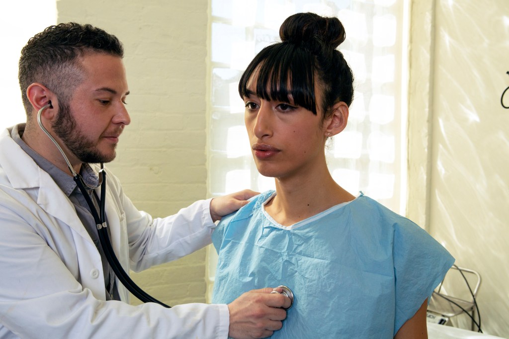 A transgender woman in a hospital gown being treated by a doctor, a transgender man