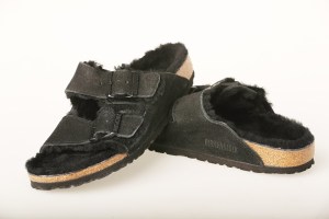 A pair of black shearling Birkenstock sandals on a white background.