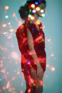 Woman standing against wall with multi-colored lights shining on her