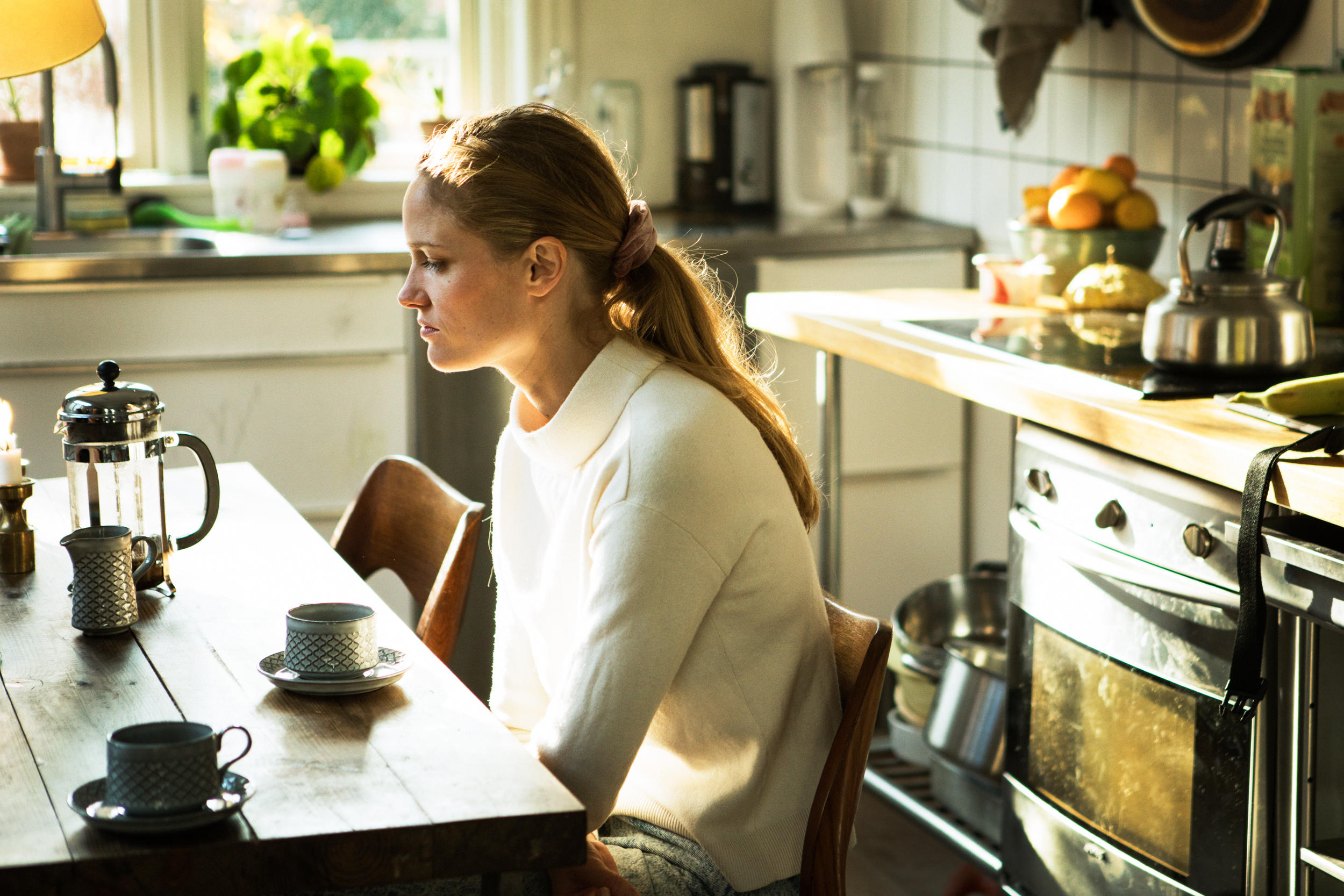 Julie sidder ved spisebordet i køkkenet og drikker kaffe