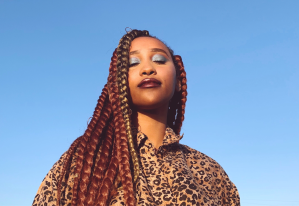 A young woman in a leopard print blouse looks at the camera, in front of a blue sky