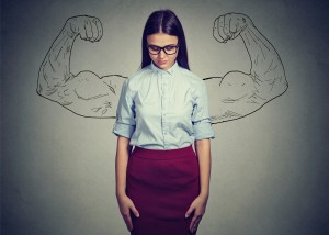 Young woman standing with a mural of big, flexing arms behind her.