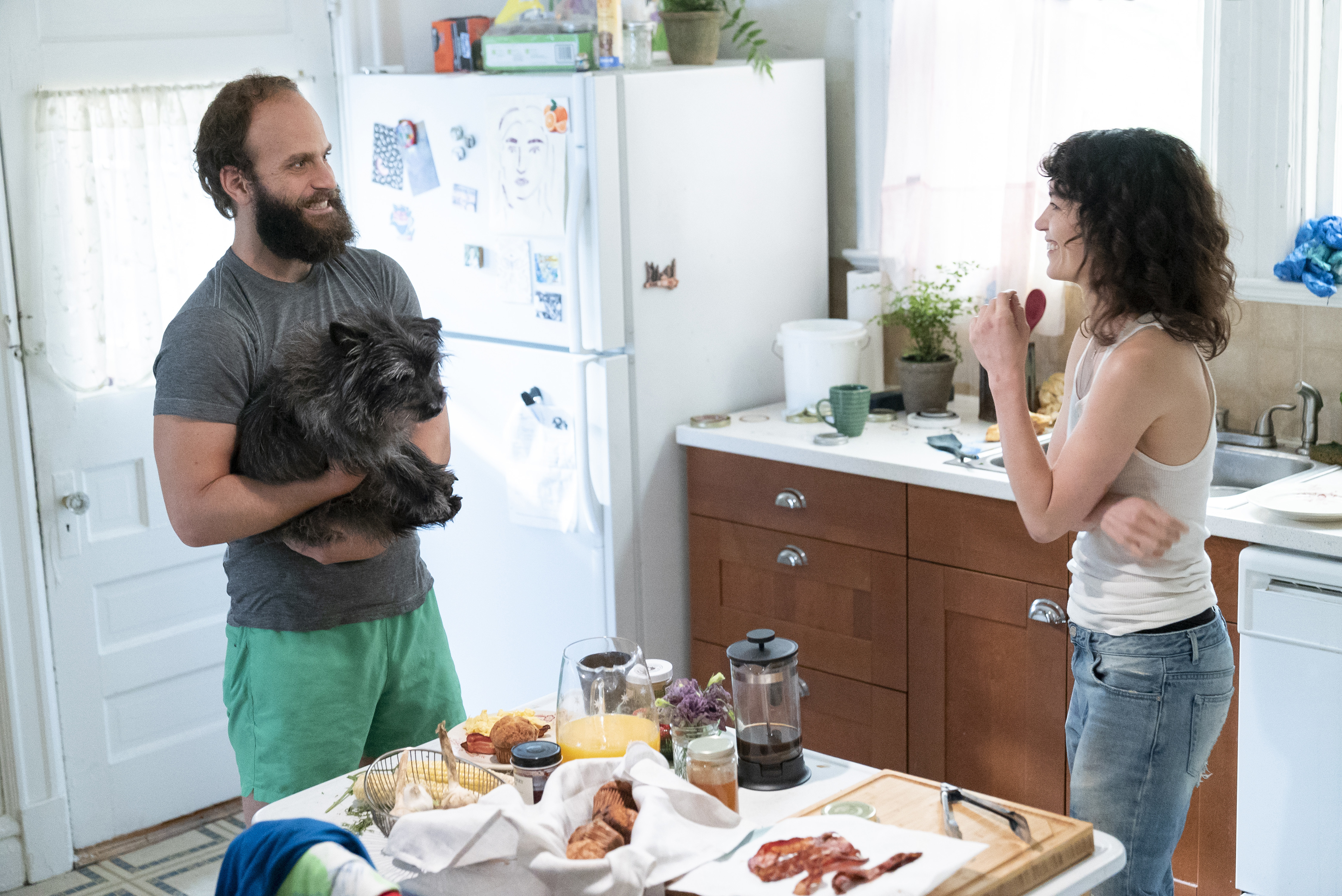 The Guy (Ben Sinclair) holds a dog in the kitchen while talking to Lee (Britt Lower) in season three of HBO's 'High Maintenance.'