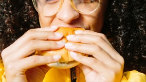 Vrouw in het geel bijt in een hamburger