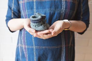 Vrouw houdt grijze babysokjes omhoog voor buik