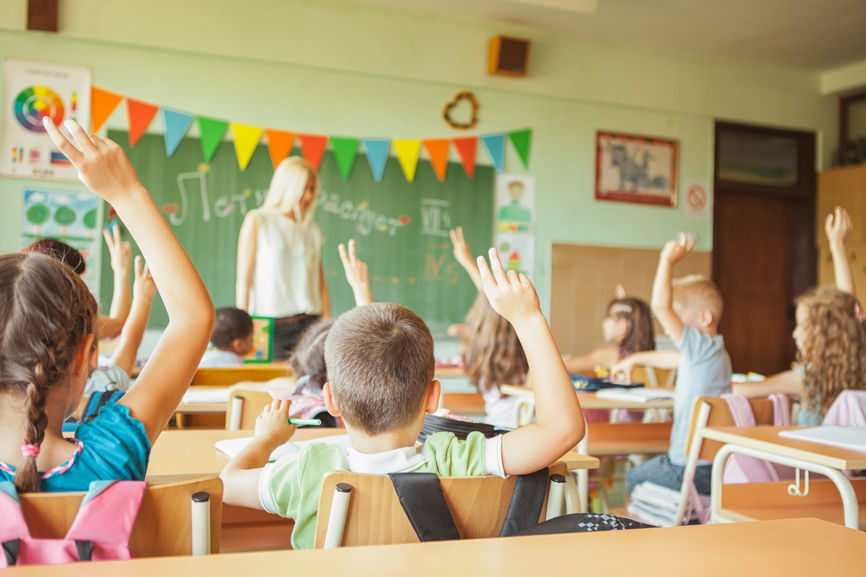 Photo of kids in school with their hands raised.