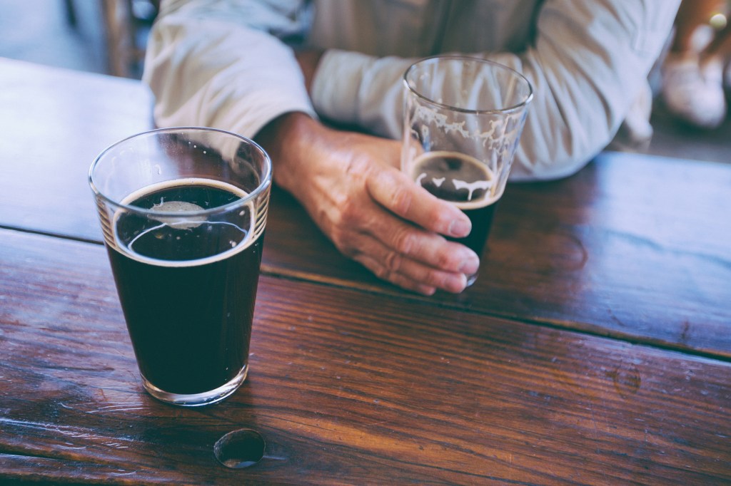 man holding a glass of beer on a wooden table