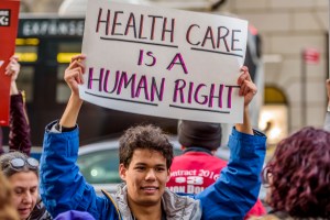 man holding a sign that says "health care is a human right"