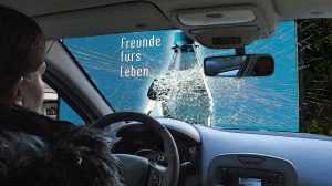 Frau am Steuer im Unfallwagen vor Plakat für nüchternes Fahren