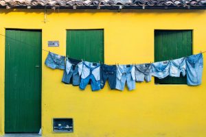 Casa simples de paredes amarelas, janelas e porta verde e roupas azuis penduradas no varal