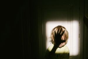 Small Child In Patch Of Light With Shadow Of Adult Hand Over Face