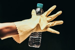 a hand in a rubber glove holding a plastic bottle of water in front of a black background