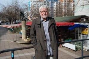 Ein älterer Mann mit weißem Haar und Bart steht an einem Marktplatz