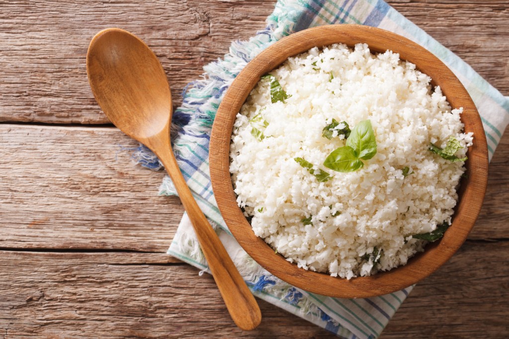 a wooden bowl of riced cauliflower topped with basil