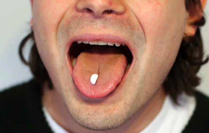 Young man with pill on his tongue