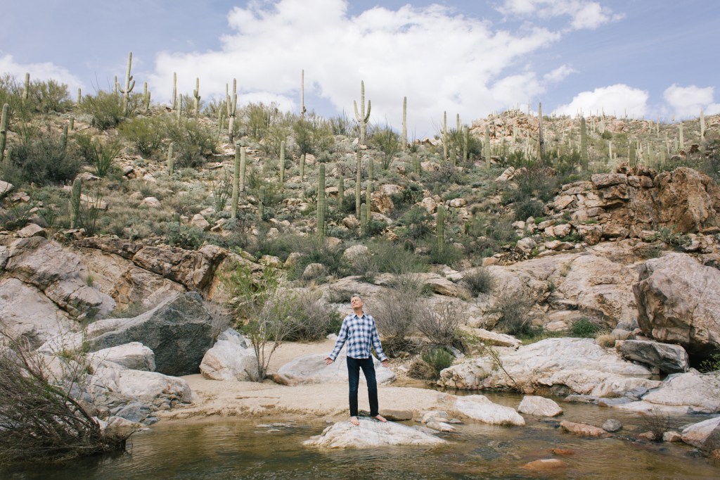 Chris Rush stands in the Arizona desert, on a rock in a river