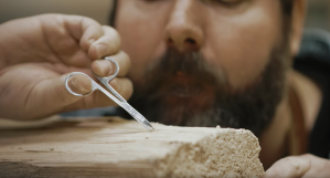 Ein Mann bearbeitet mit einer Nagelschere einen Holzblock