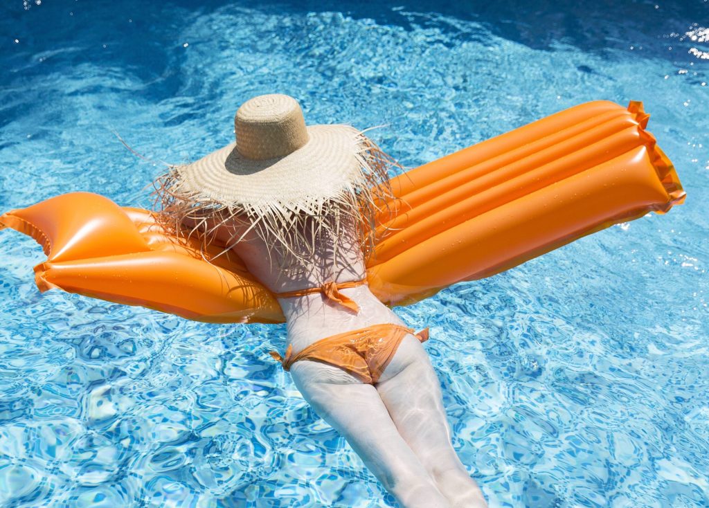 Eine Frau in einem orangefarbenen Bikini und Strohhut schwimmt auf einer Luftmatratze