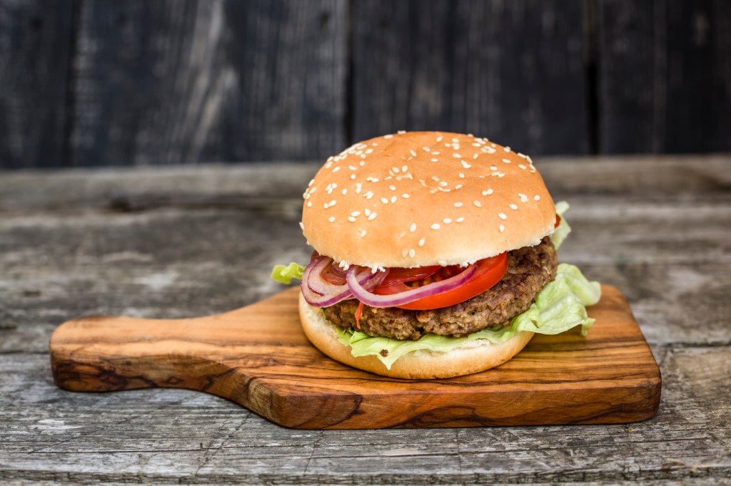 veggie burger topped with red onions and tomatoes on a wooden board