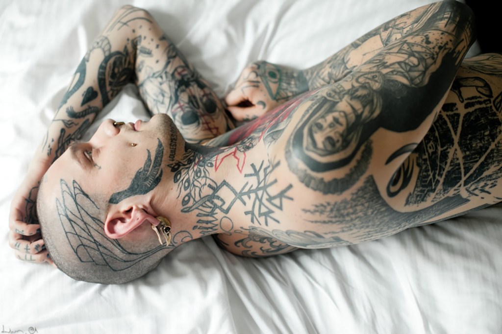 A tattooed man with shaved head lying on bed