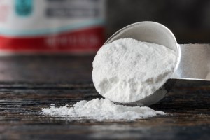 Steel measuring spoon of baking soda spilling onto table