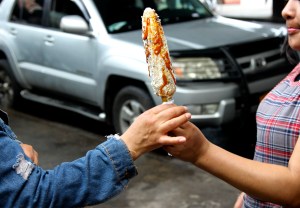 Queens street vendor hands elotes to a customer