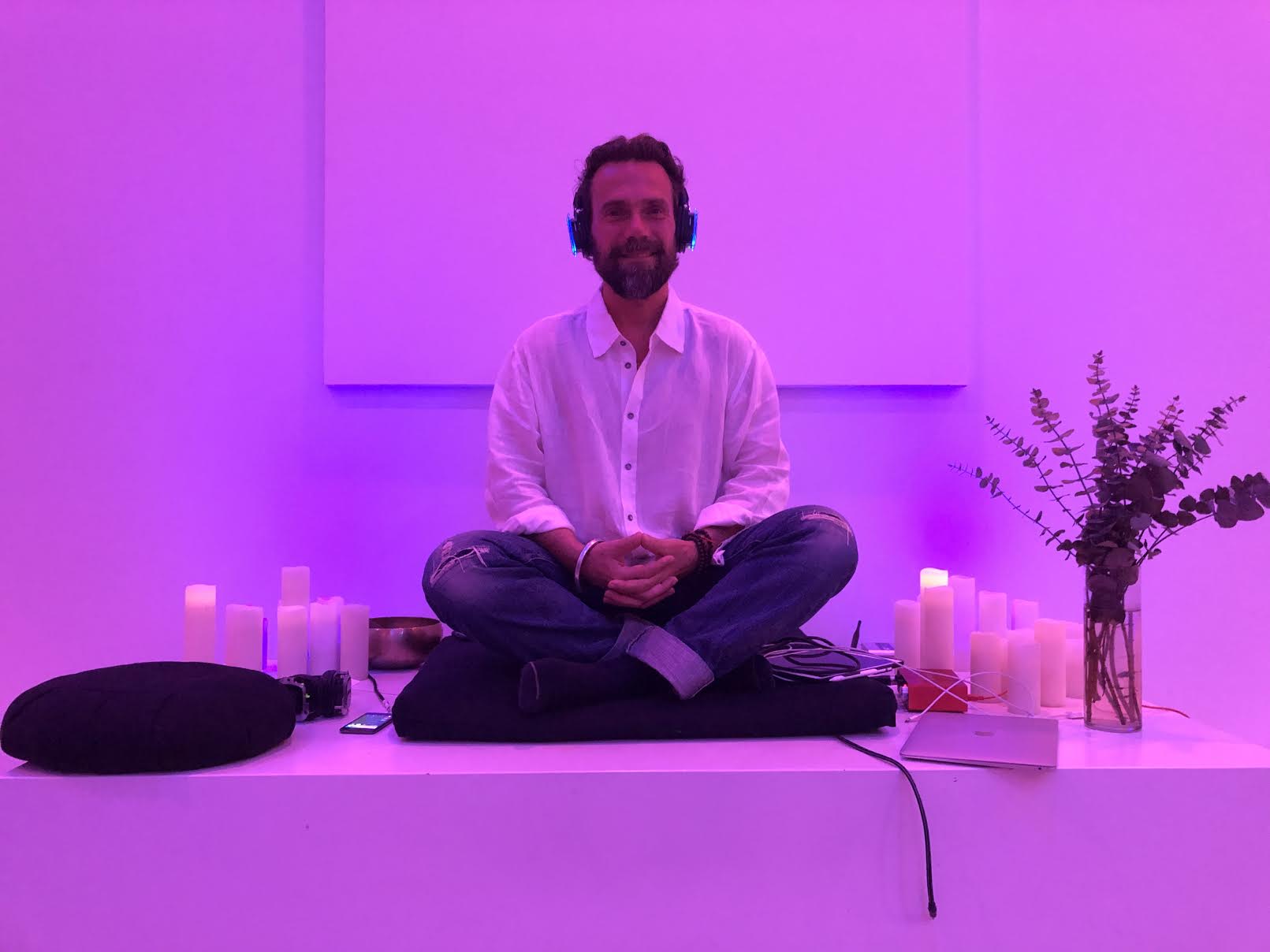 A man sits crosslegged bathed in purple light