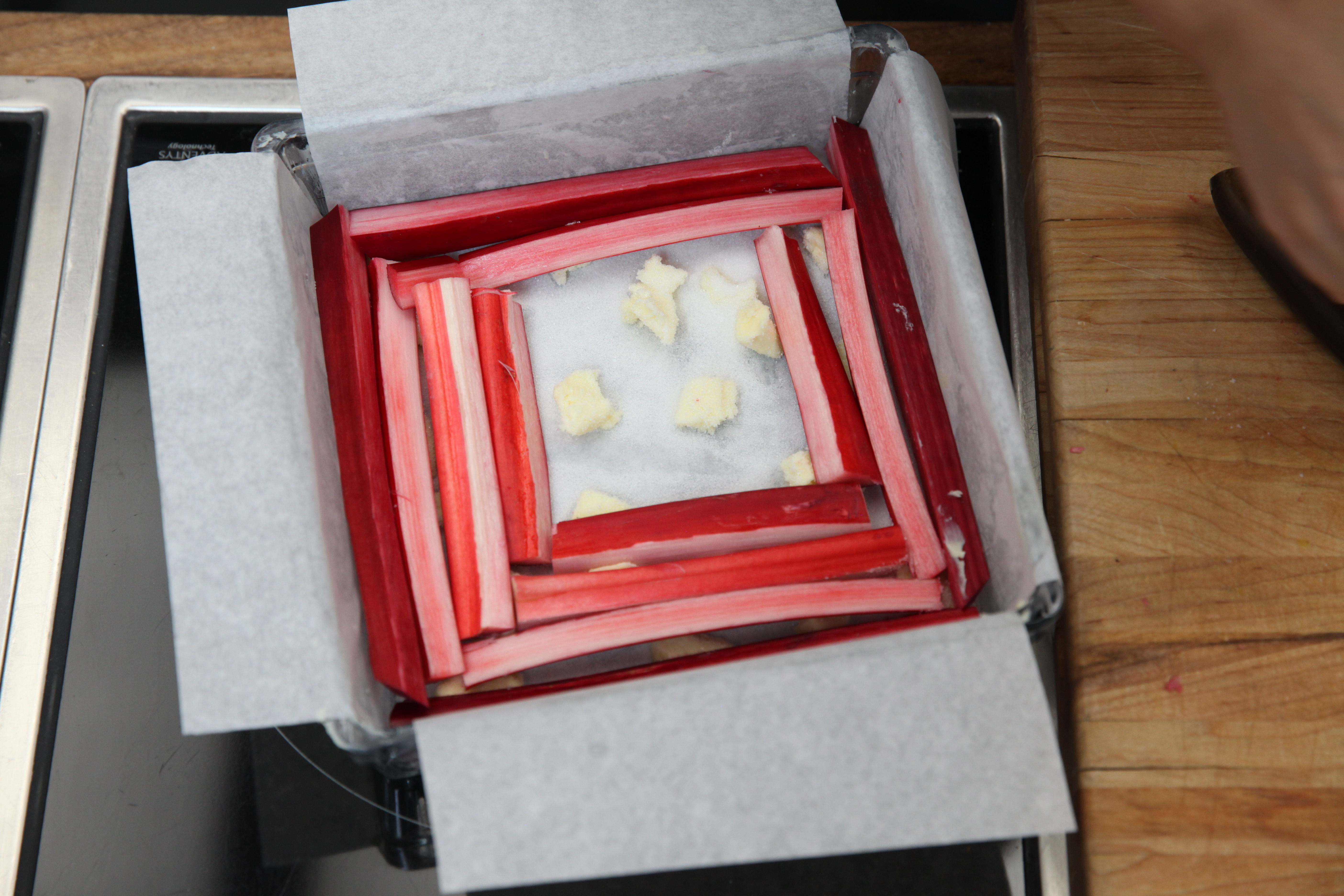 a cake pan lined with parchment paper and topped with butter, white sugar, and stalks of rhubarb