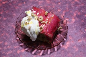 a pink glass plate topped with a slice of janine booth's rhubarb upside-down cake, rosewater whipped cream, and orange syrup