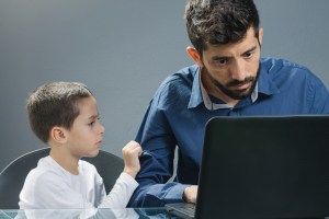 Father on laptop ignoring son while the child tries to catch his attention.