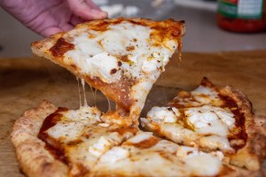 a hand pulling up a slice of gluten-free cheese pizza