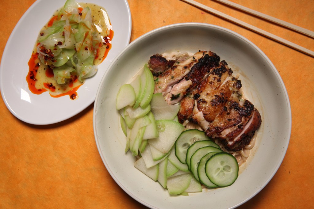 a plate of spicy, raw chayote salad to the left of a plate of sesame noodles topped with seared chicken thighs, cucumber, and seared chayote