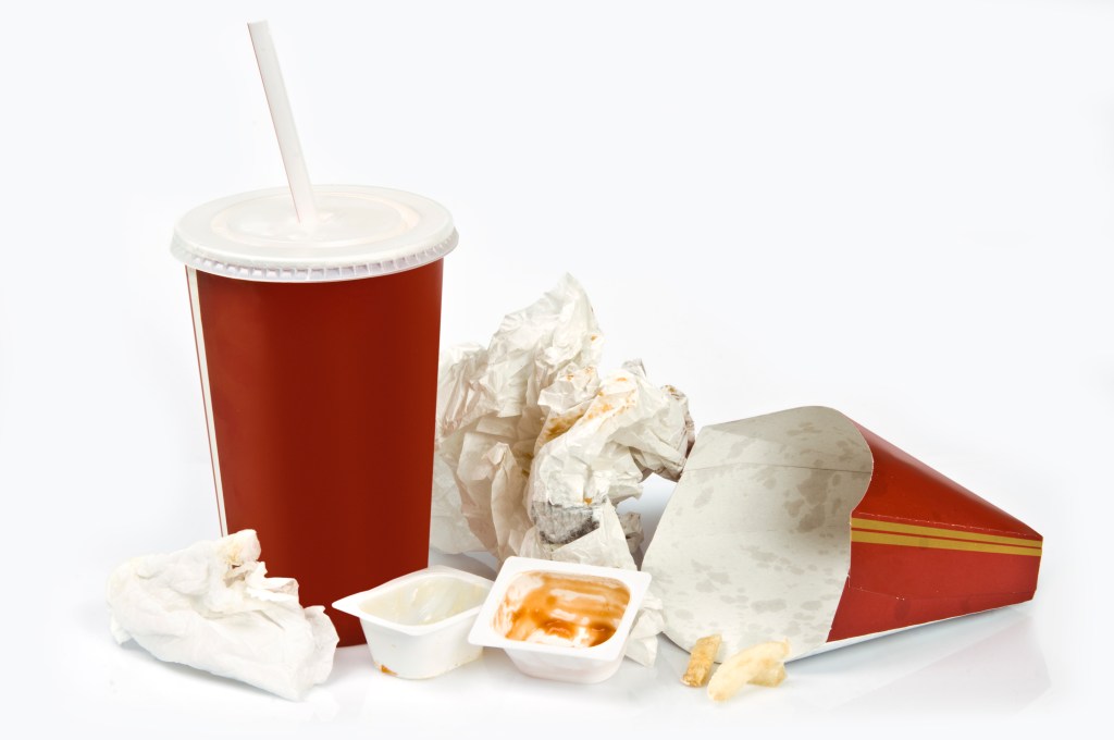 a collection of unbranded fast food trash, including a red paper cup with straw and an empty, greasy french fry container