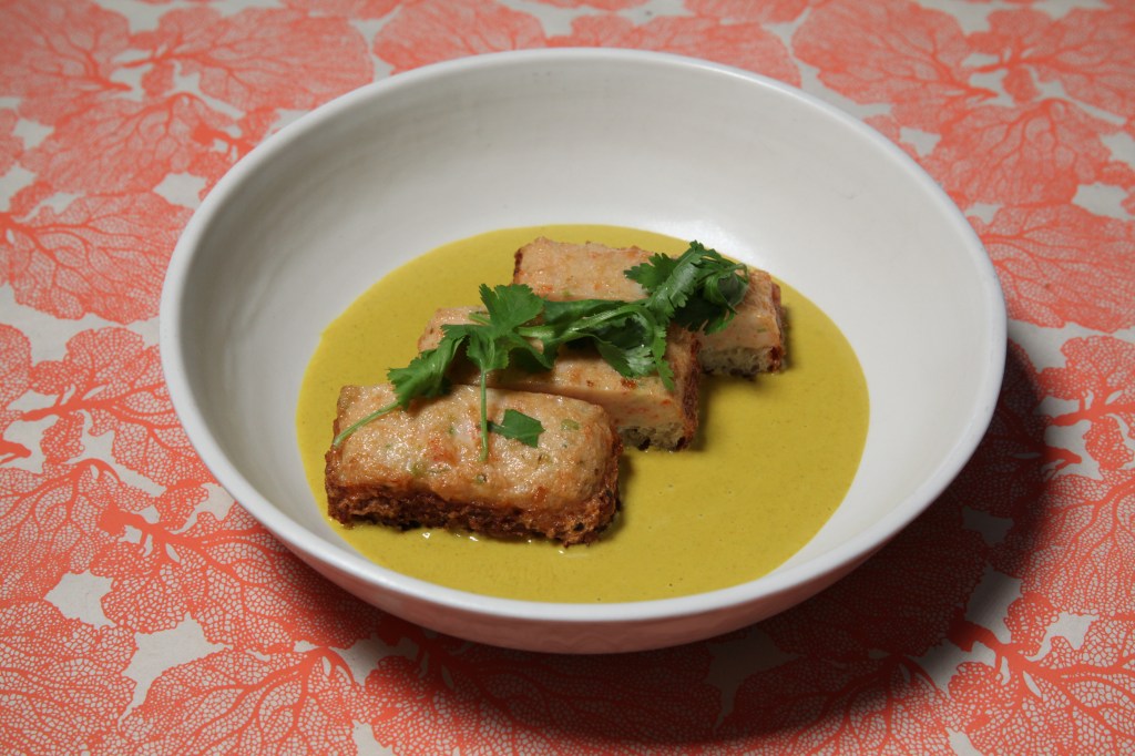 a white bowl of shrimp toast on top of yellow cantonese curry from chef mei lin of nightshade in los angeles