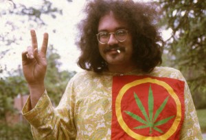 John Sinclair wears an outfit with a cannabis leaf on it and gives the peace sign.