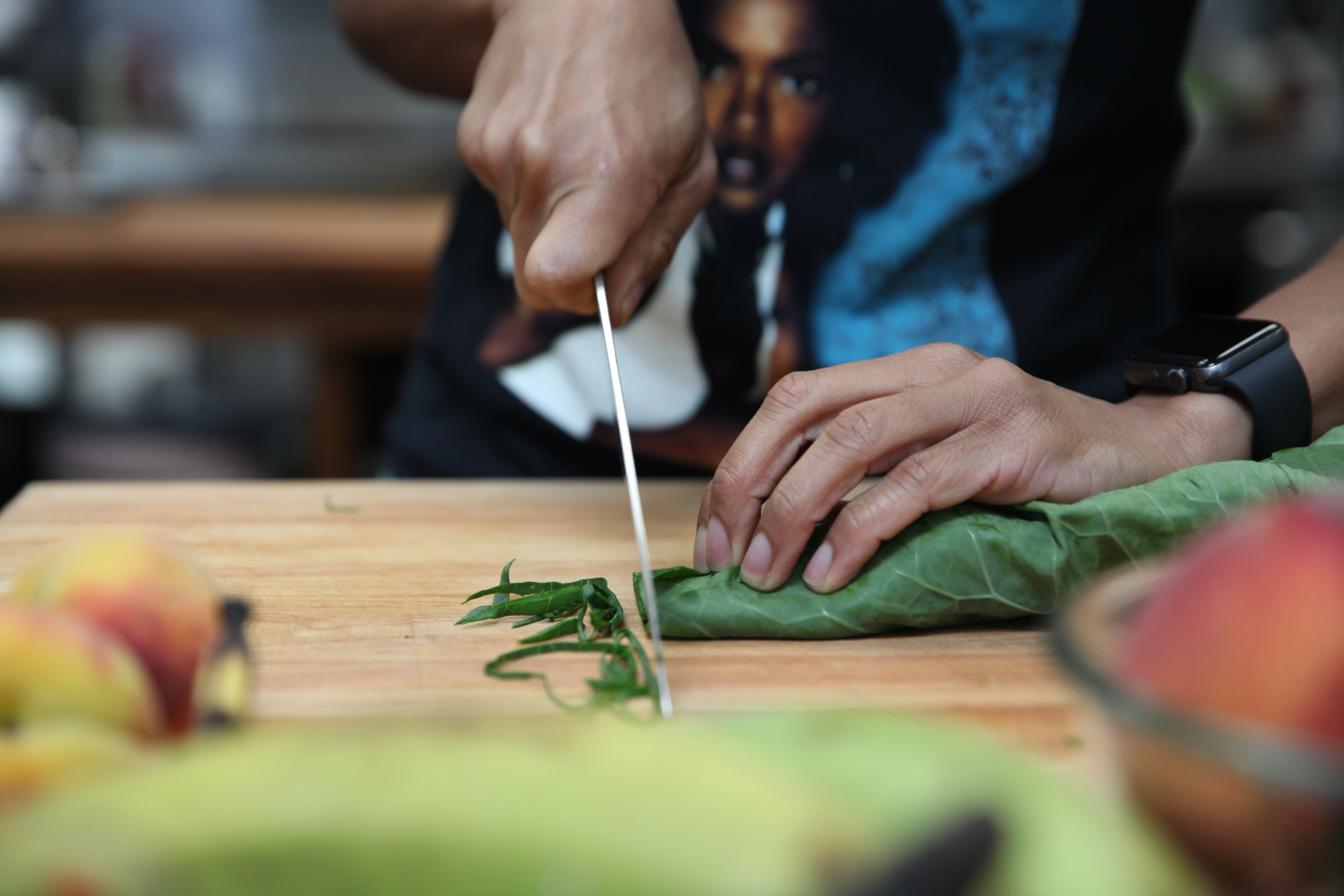 chef ashleigh shanti julienning collard greens for a salad, with a lauryn hill t-shirt in the background